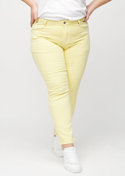 Lysegule slim jeans, modelnavn Lemonades, som sidder tæt til benet, dog lidt løsere ved anklen, på en plus-size model, set forfra.